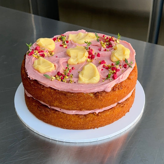A vanilla buttermilk sponge cake with a raspberry cream cheese frosting filling and topping with dollops of lemon curd, a sprinkling of pistachio, freeze dried raspberry and thyme to decorate.