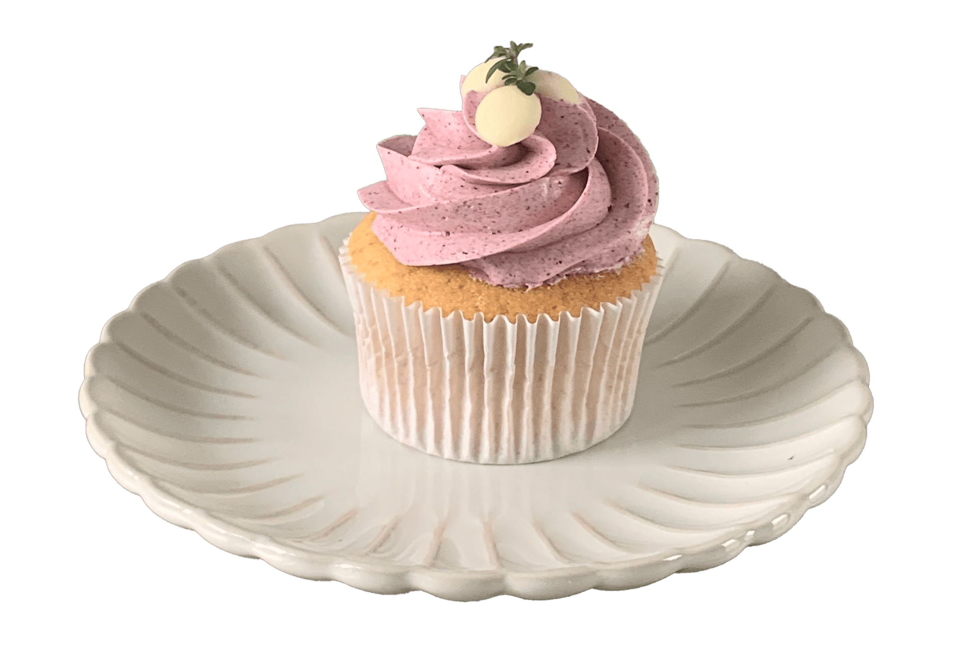 Placed on a white vintage style plate is a vanilla sponge cupcake topped with freeze dried Boysenberry in a Swiss meringue buttercream. Garnished with Belgian white chocolate drops.