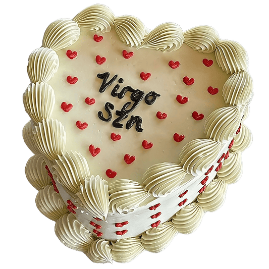 A heart shaped vintage style cake in white Swiss Meringue buttercream with piped shells around the top and bottom.  Dainty red hearts are piped on the top and sides of the cake with a piped written message in the middle.